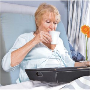 Bed wedge supporting elderly lady drinking tea in hospital bed